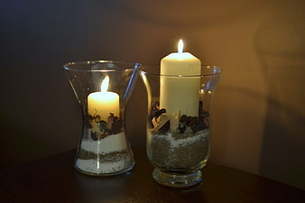 Two lit candles in glass vases with sand and dried flowers