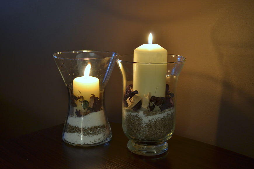 Two lit candles in glass vases with sand and dried flowers