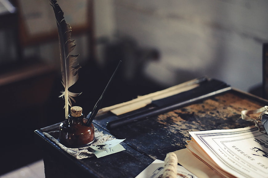 Vintage quill pen and ink bottle on rustic wooden desk