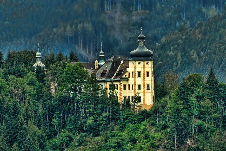 Historic yellow castle nestled in dense green coniferous forest