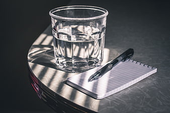 Glass of water and notepad on desk with sunlight