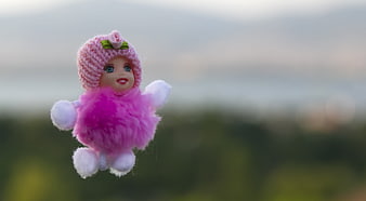 Cute pink doll toy with knitted hat and fluffy outfit against blurred background