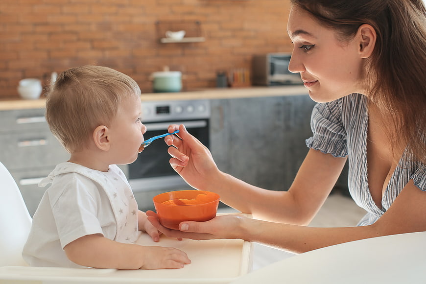 Mother feeding baby puree in modern kitchen