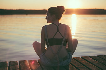 Woman meditating on wooden dock at sunset