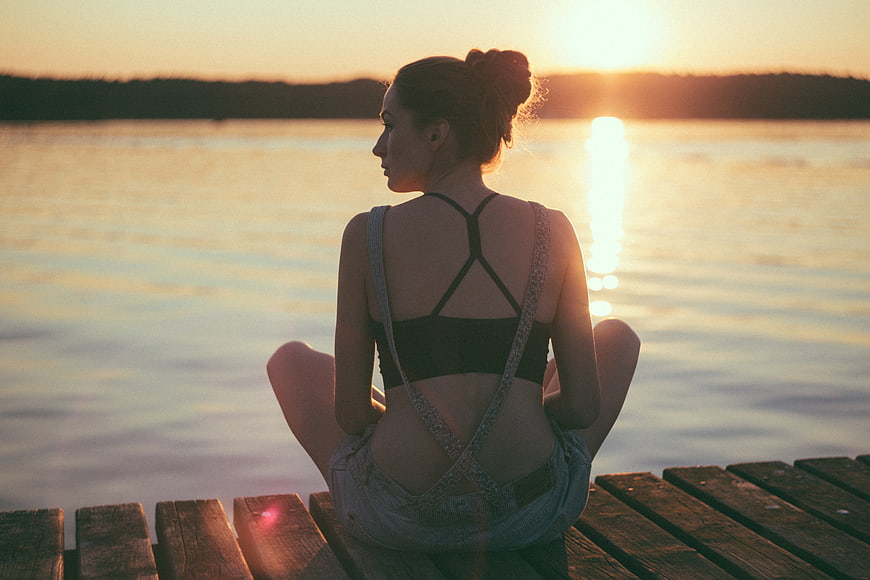 Woman meditating on wooden dock at sunset