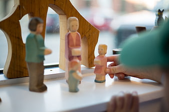 Child Playing with Wooden Family Figures on Windowsill