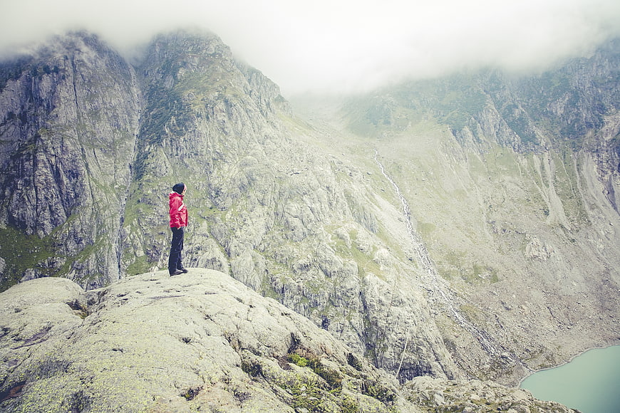 Hiker in Red Jacket Standing on Mountain Peak Overlooking Valley
