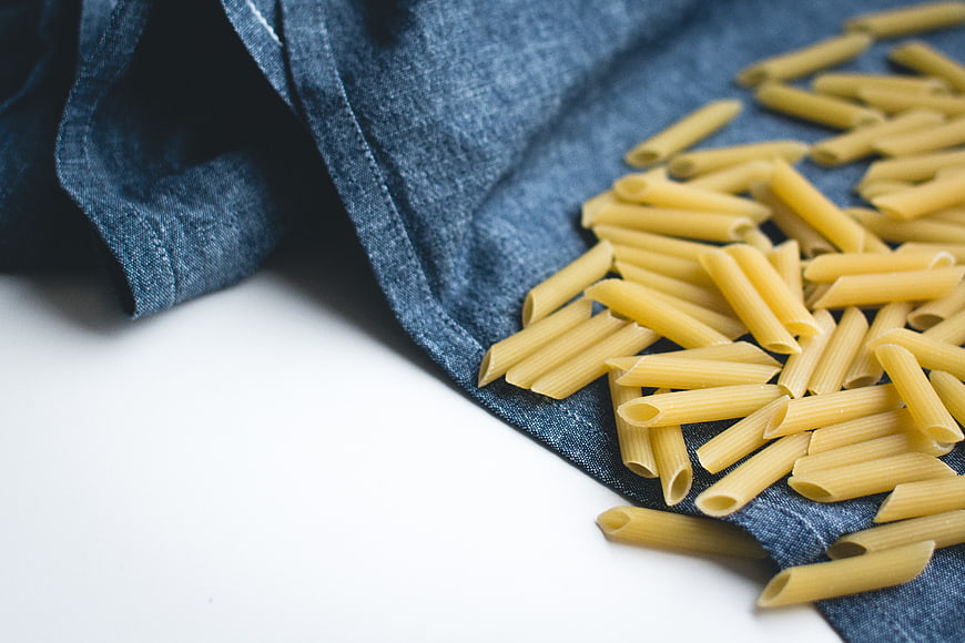 Uncooked penne pasta on blue linen cloth
