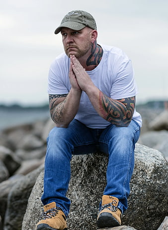 Contemplative tattooed man sitting on rock by the sea