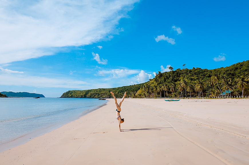 Woman doing handstand on tropical beach with palm trees
