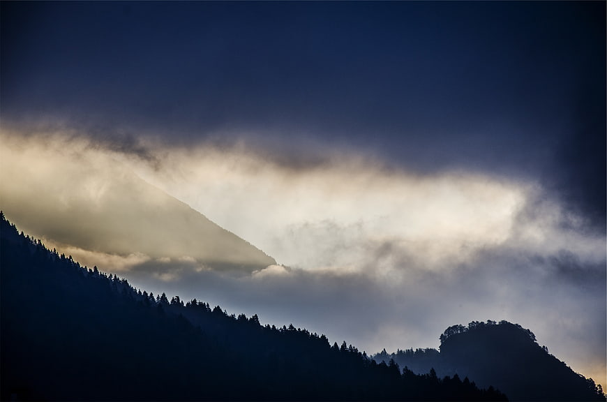 Dramatic Mountain Landscape with Sunlit Clouds and Silhouetted Trees