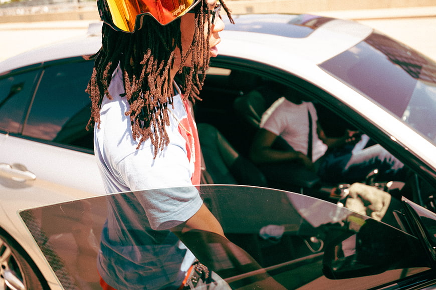 Man with dreadlocks and sunglasses getting into a white car