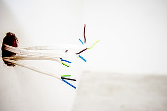 Exposed electrical wires protruding from a white wall socket hole