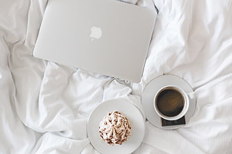 Laptop, coffee, and dessert on white bed sheets