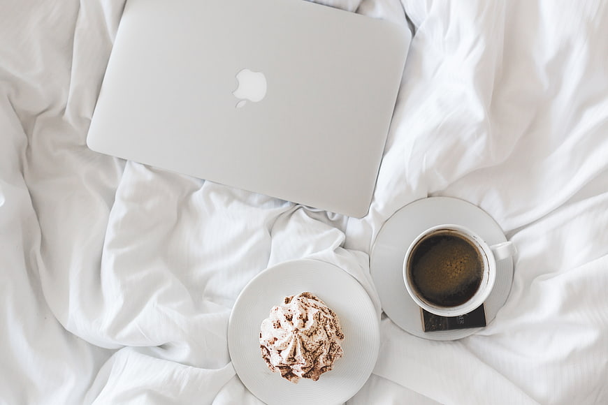 Laptop, coffee, and dessert on white bed sheets