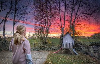 Girl watching colorful sunset over autumn garden with playhouse