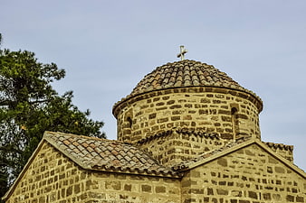 Ancient stone church dome with cross against blue sky