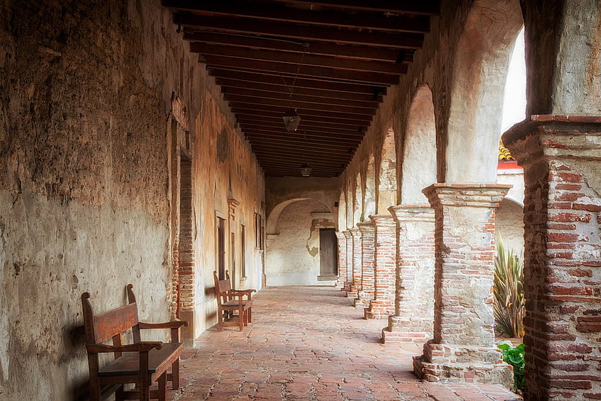 Historic Mission Corridor With Arched Columns And Wooden Benches