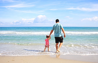 Father and daughter holding hands walking on sunny beach
