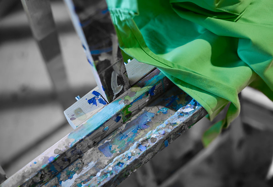 Close-up of wooden easel with green cloth and paint splatters