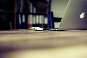 Silver laptop and mouse on wooden desk with blurred bookshelf background