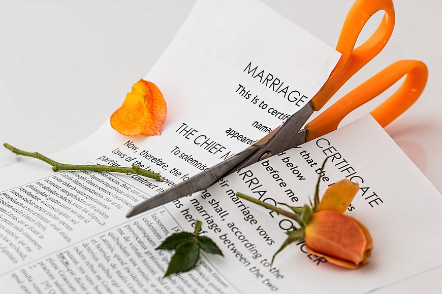 Scissors cutting marriage certificate with dried rose petals