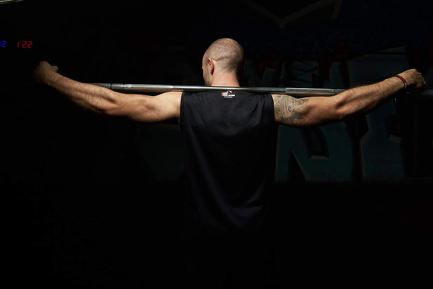 Back view of muscular man holding barbell in dark gym