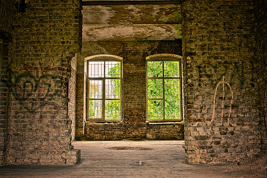 Interior of Abandoned Brick Building with Arched Windows and Overgrown Greenery