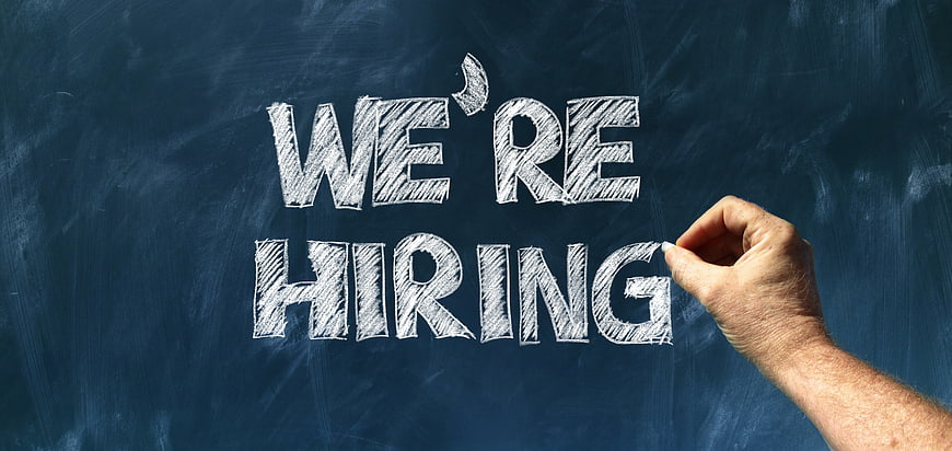 Hand writing We're Hiring in chalk on a dark blue blackboard