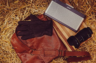 Leather bag, gloves, camera lens, and speaker on straw