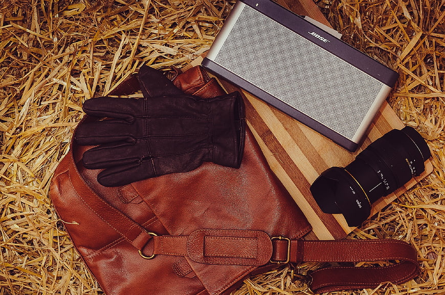 Leather bag, gloves, camera lens, and speaker on straw