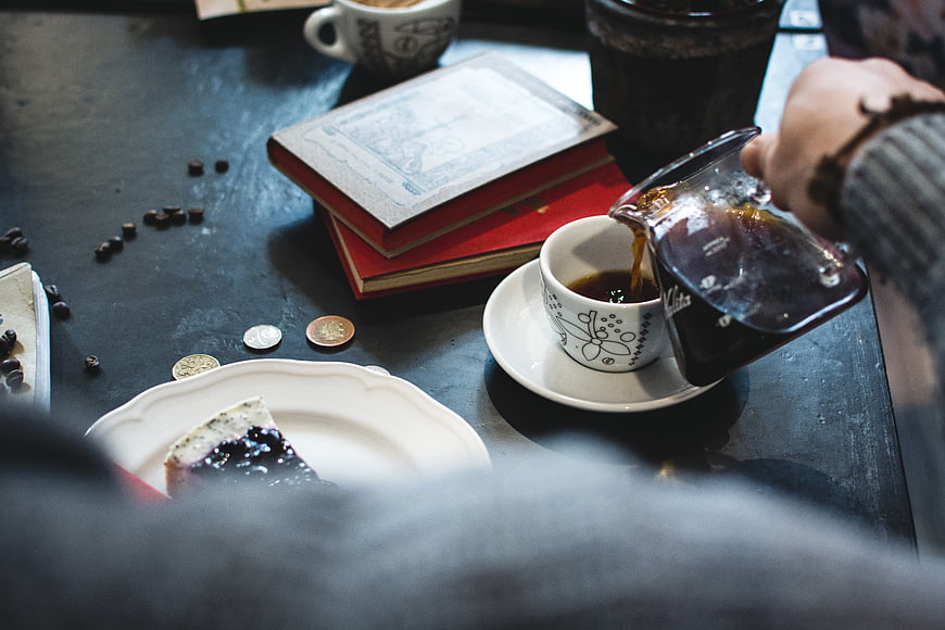 Pouring black coffee into a cup with books and cake