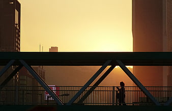Silhouette of Person Walking on Urban Bridge at Sunset