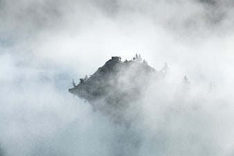 Misty mountain peak with cabin emerging from clouds