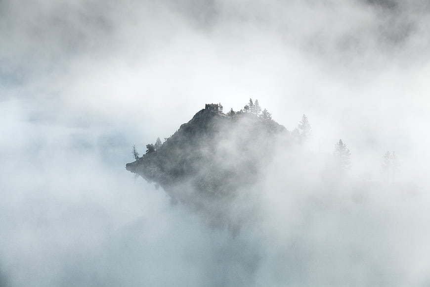 Misty mountain peak with cabin emerging from clouds