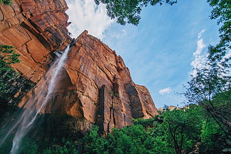 Majestic waterfall cascading down red rock cliff with lush green trees