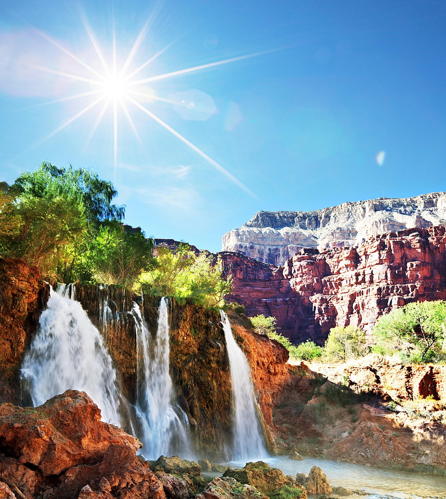 Sunlit waterfall cascading into red rock canyon