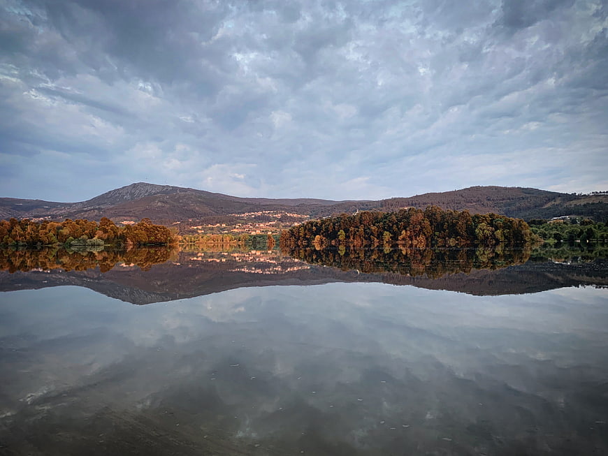 Serene Lake Reflection with Autumn Hills and Cloudy Sky
