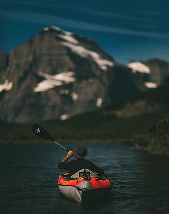 Man kayaking on lake with snow-capped mountain background