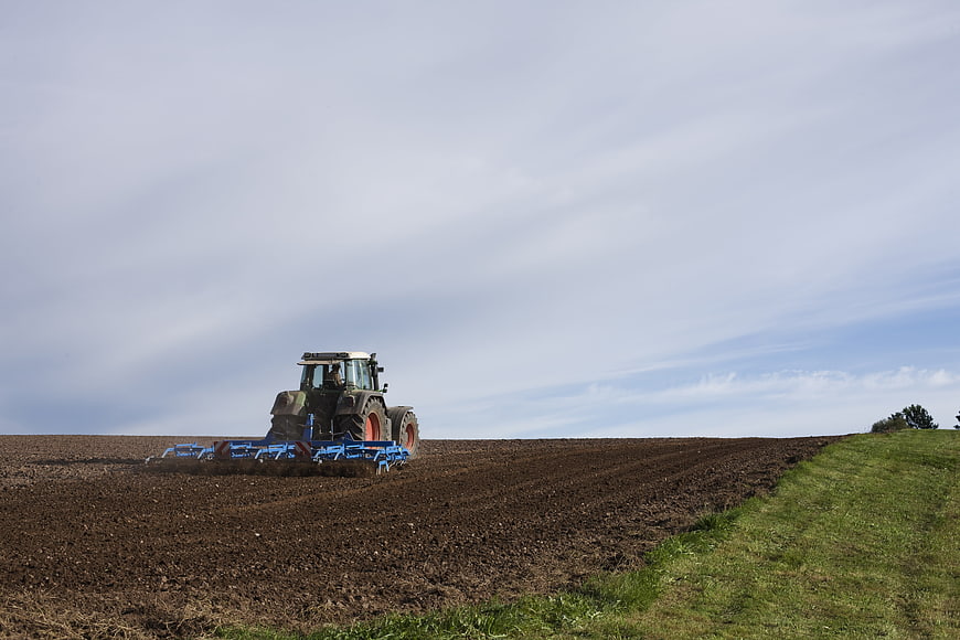 Green tractor plowing a brown field under a cloudy sky
