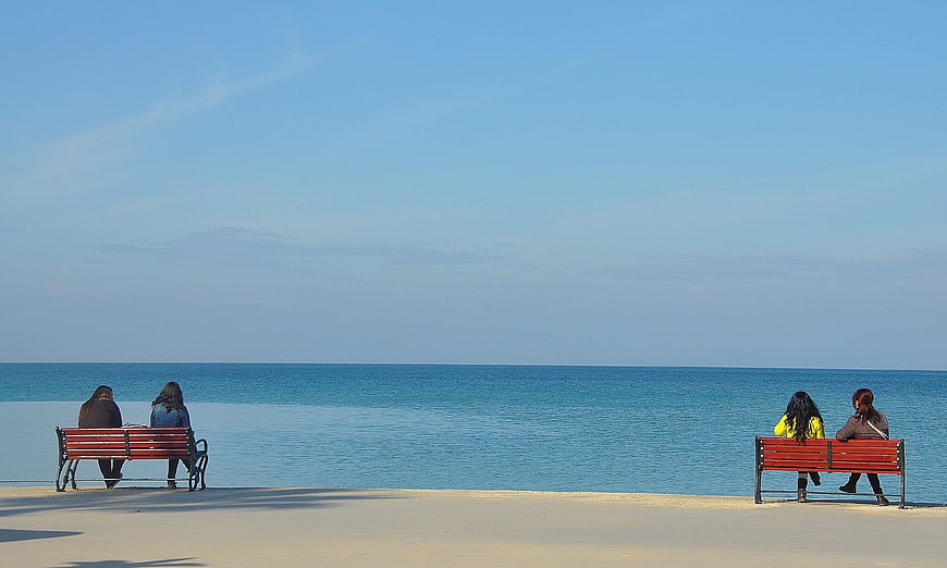 Couples sitting on red benches overlooking calm blue sea
