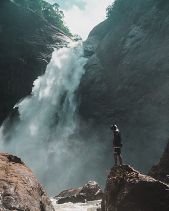 Man standing on rock near powerful waterfall in nature