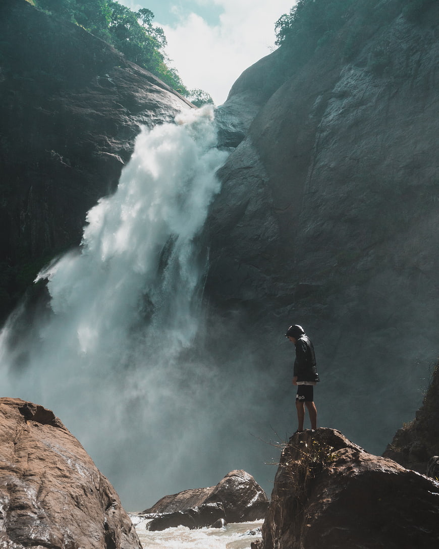 Man standing on rock near powerful waterfall in nature