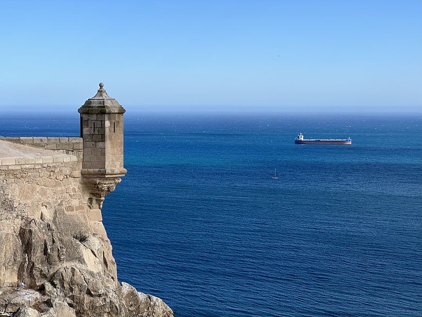 Historic stone tower on cliff overlooking blue sea with cargo ship