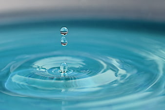 Macro shot of water droplets falling into blue water creating ripples