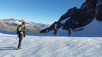 Three mountaineers roped together hiking on a snowy glacier