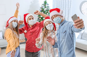 Happy friends taking selfie with masks and Santa hats at Christmas