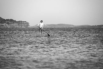 Man paddleboarding on calm ocean water in black and white