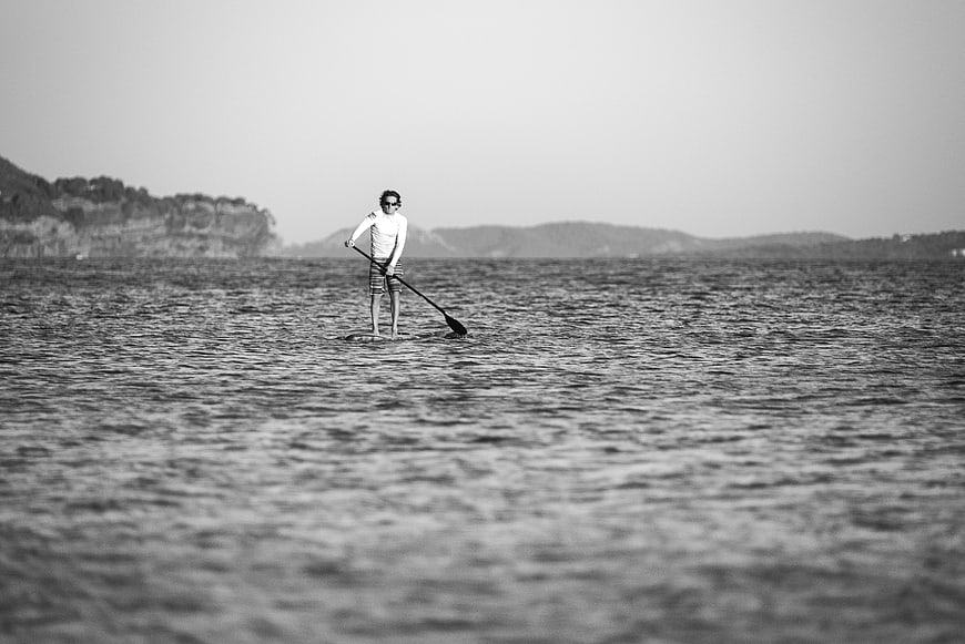 Man paddleboarding on calm ocean water in black and white