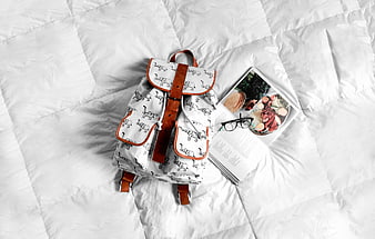 Flat lay of white elephant print backpack with book and glasses
